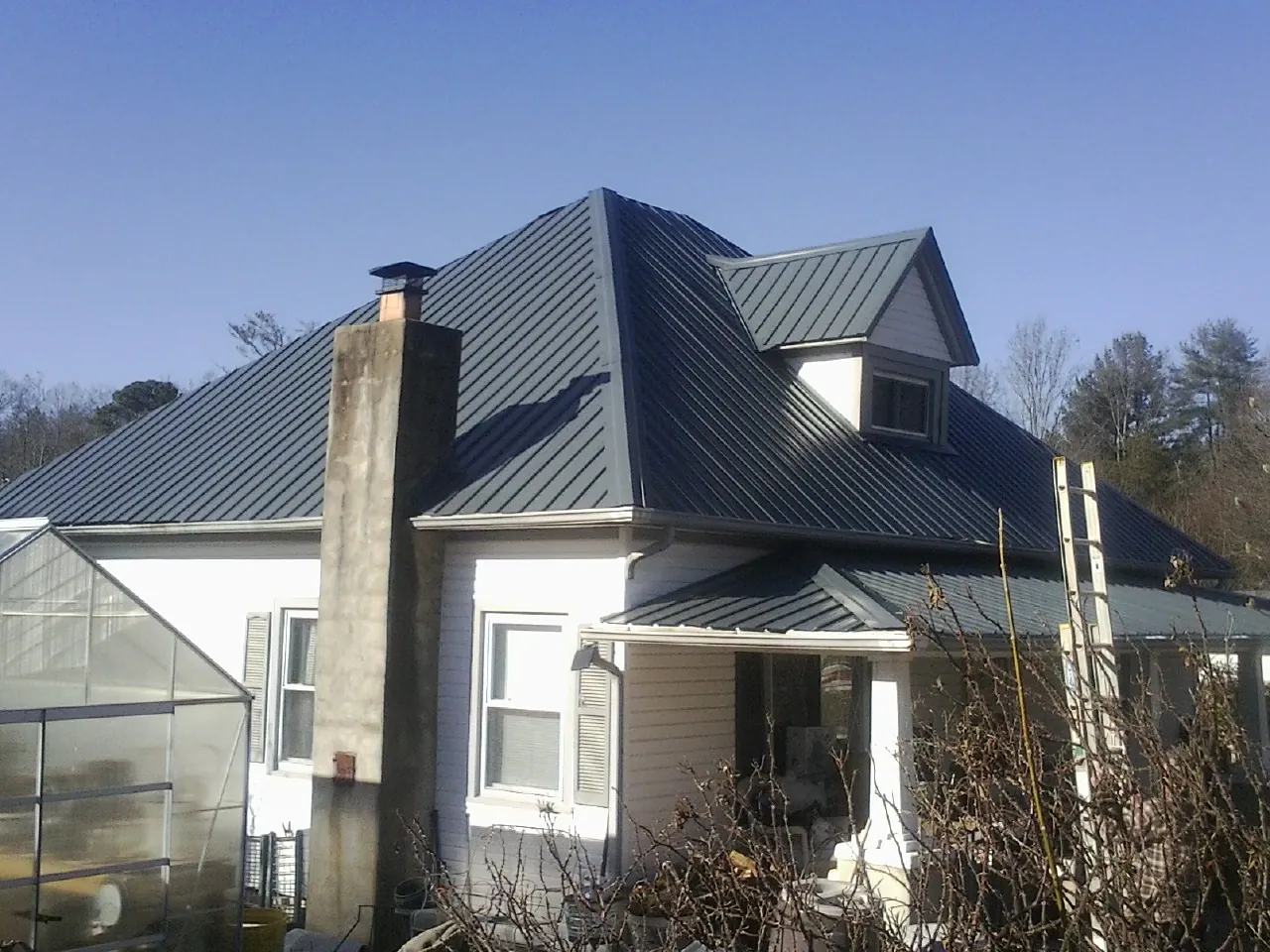 Dark blue standing seam metal roof on a white farmhouse with dormer — Slate & Tile Roof Repair by Roofing Brothers in Cedar Vale