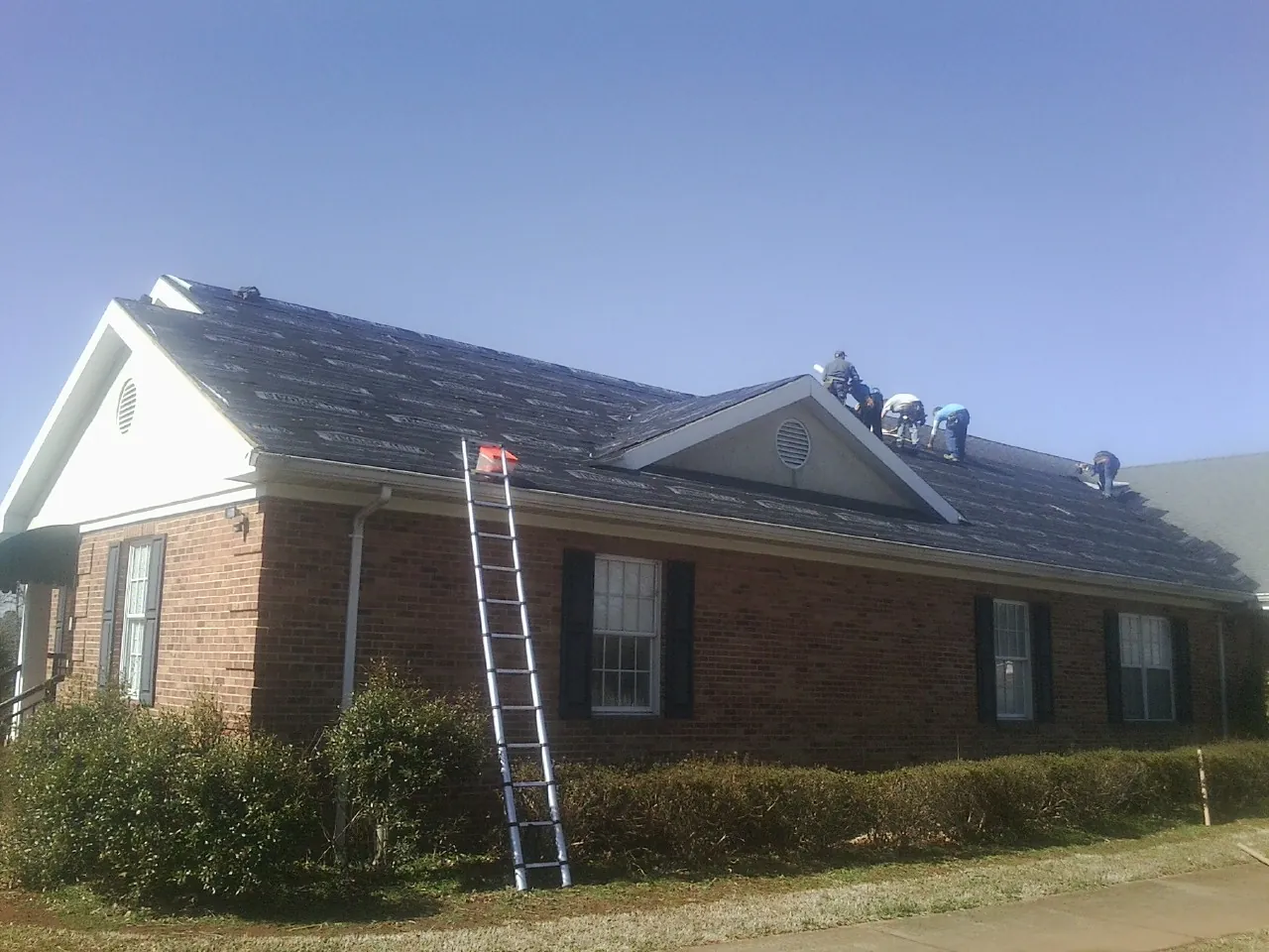Crew tearing shingles off a brick ranch roof with a ladder set — Emergency Roof Repair work by our crew in Cedar Vale