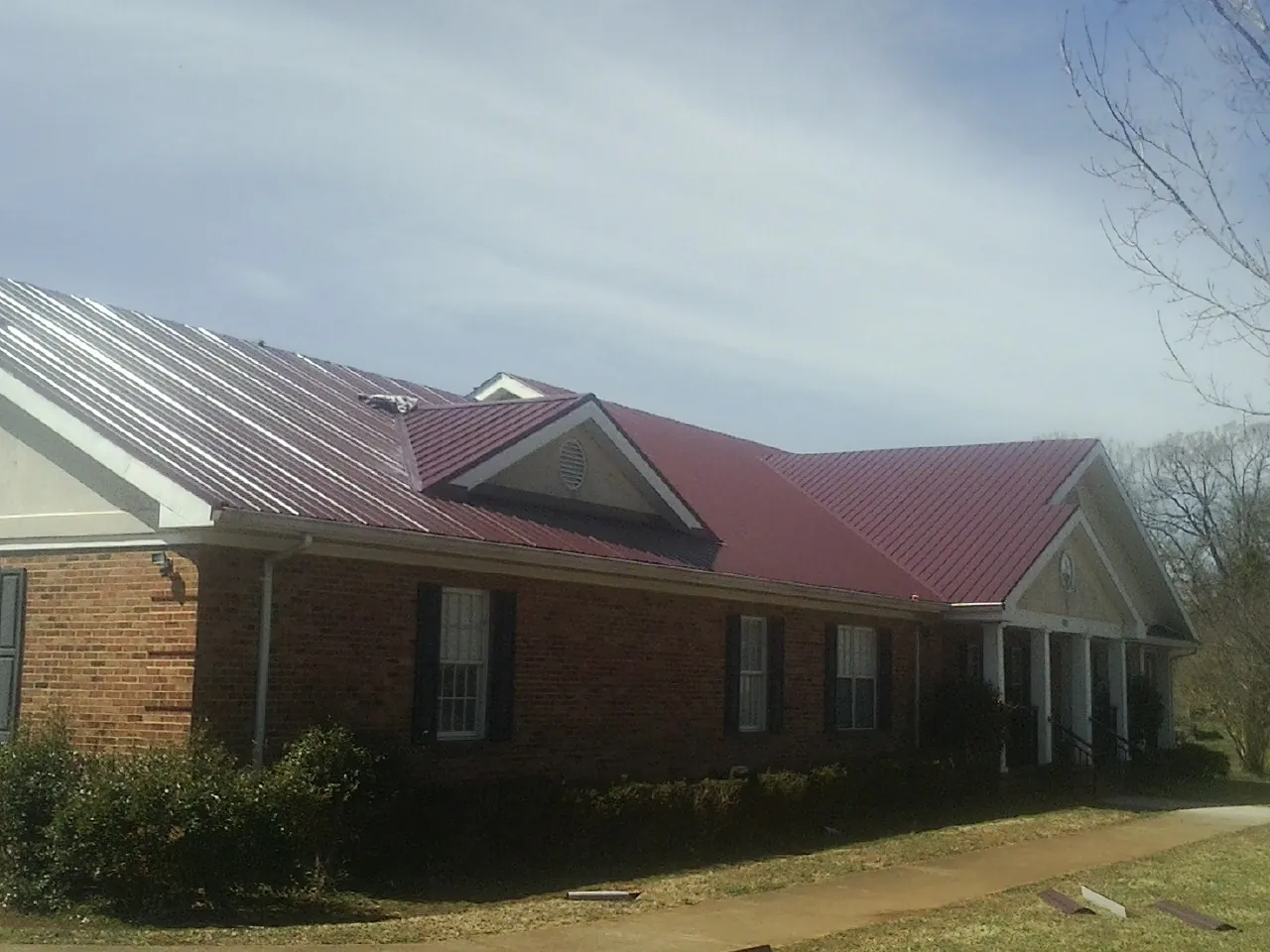 Red metal roof with gabled entries on a long brick building, from a Hail Damage Roof Repair job in Cedar Vale