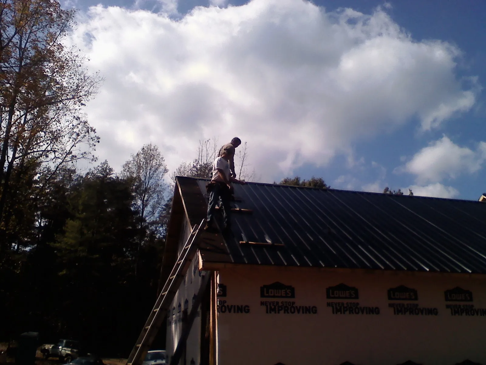 Roofer fastening dark metal panels high against a cloudy sky, from a Roof Inspection job in Cedar Vale