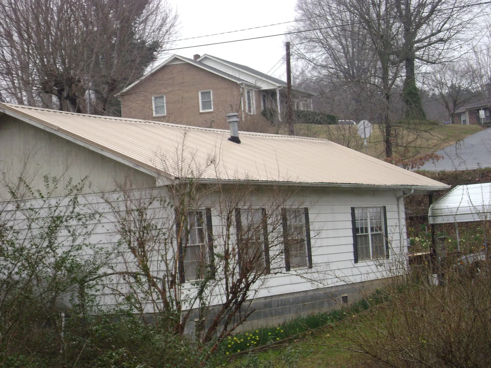 Tan metal roof on a white sided house set into a hillside — Commercial Roofing by Roofing Brothers in Cedar Vale