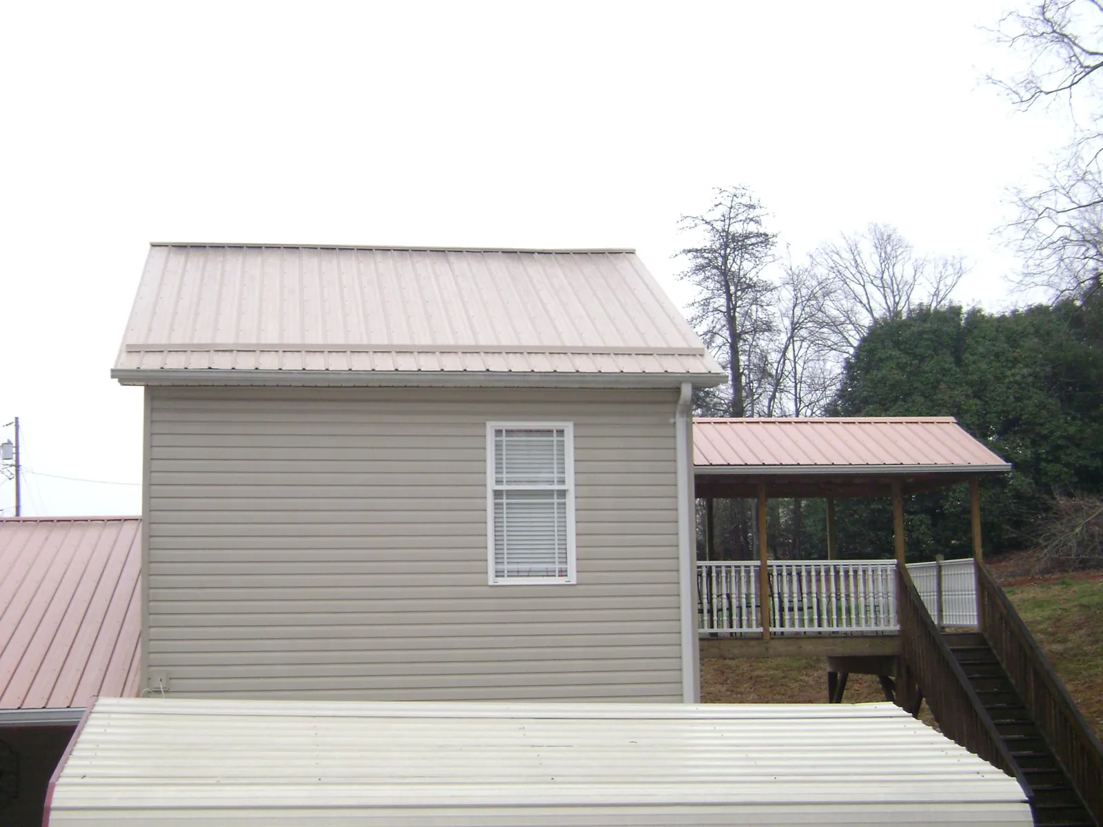 Tan metal roofs on a two story addition and attached porch, from a Roof Replacement job in Cedar Vale